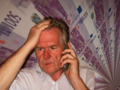Symbolfoto zum Thema "Unseriöse Telefonwerber" - gestresster Mann am Telefon, im Hintergrund Geldscheine