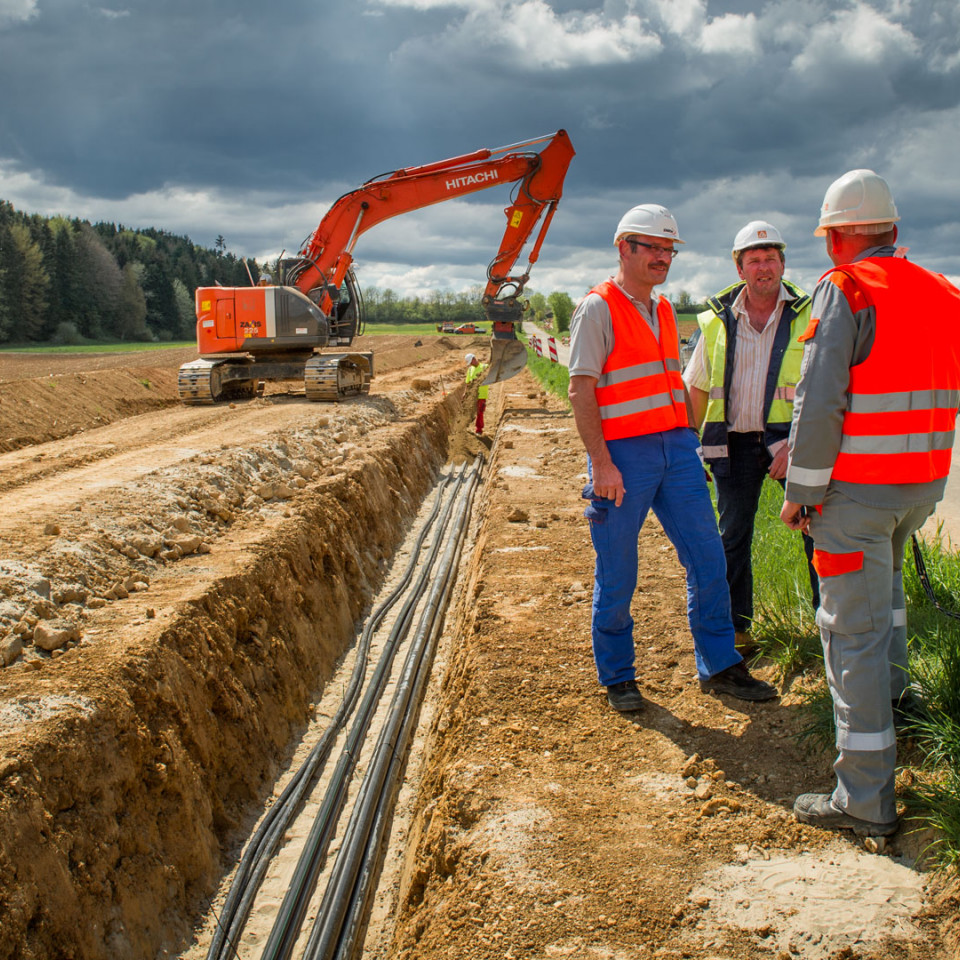 Stromnetzverlegung - Drei Mitarbeiter mit Bagger
