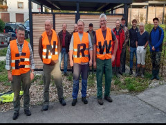 Vier Männer mit Warnwesten mit Aufschrift ENRW, dahinter weitere Männer