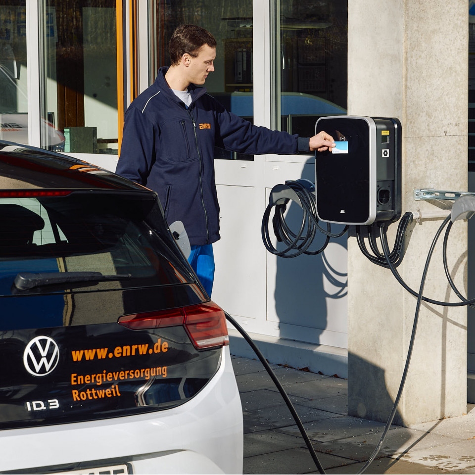 E-Auto lädt an Ladesäule, Fahrer hält Karte an Ladesäule